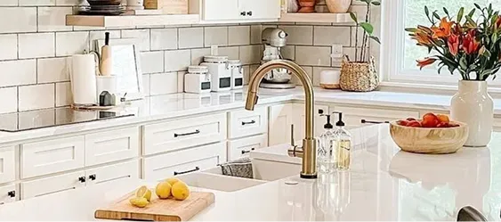 Beautifully decorated kitchen with cream cabinets, cream tile backsplash, cream kitchen island, and champagne bronze Delta faucet over double sink.